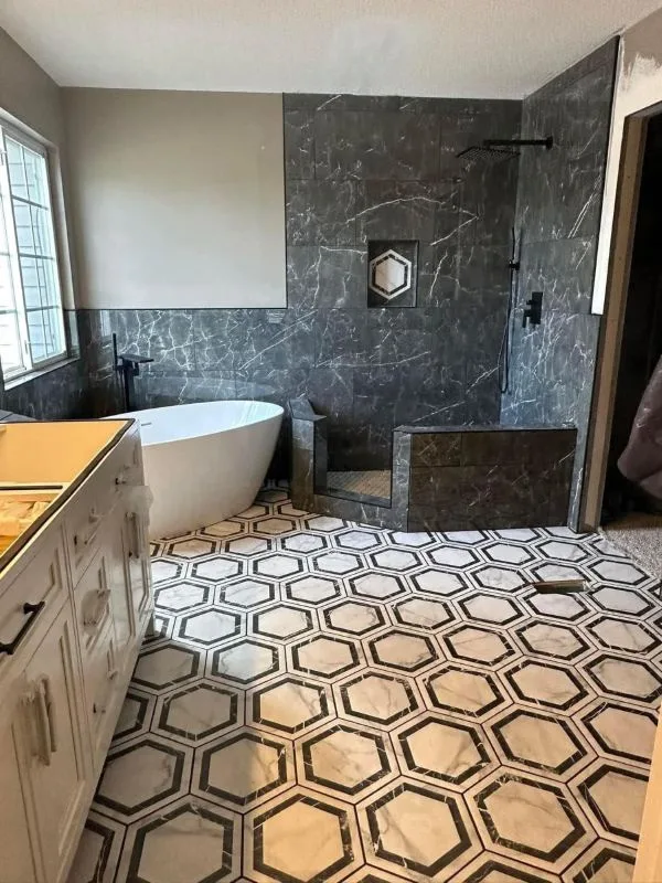 Completed bathroom renovation with a freestanding tub, dark marble wall and hexagon tile floor